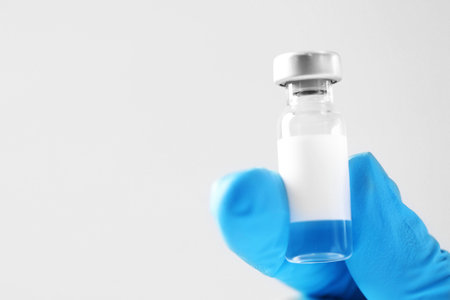 Nurse holding vial of vaccine on light background, closeup. Space for text
