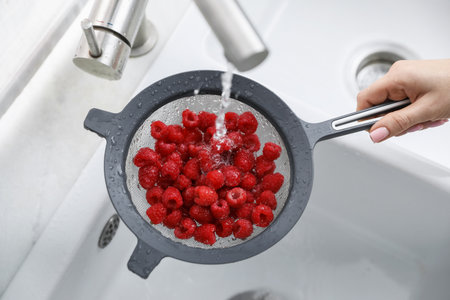 Woman washing raspberries in sieve at sink, closeup