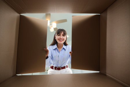 Woman opening cardboard box against ceiling in room, view from inside package
