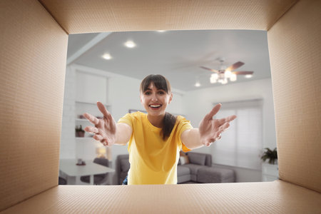 Woman looking into cardboard box in room, view from inside package