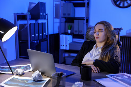 Tired woman sleeping at workplace in office at nightの写真素材