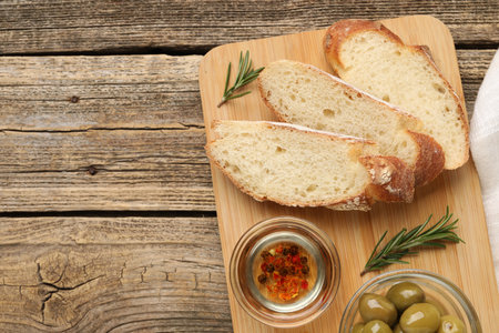 Slices of baguette with oil, spices and olives on wooden table, top view. Space for text