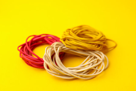 Many colorful rubber bands on yellow background, closeup