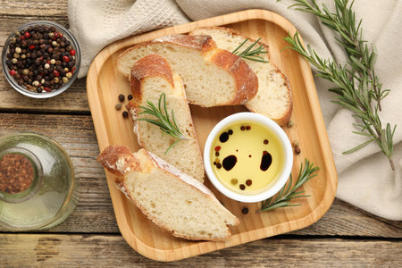 Slices of baguette with olive oil, rosemary and spices on wooden table, flat layの写真素材