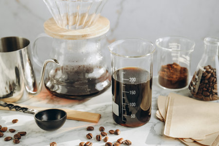 Tasty drip coffee, beans, laboratory glassware, kettle, paper filters and chemex coffeemaker on...