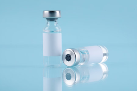 Vaccine in glass vials on mirror surface against turquoise background, closeup
