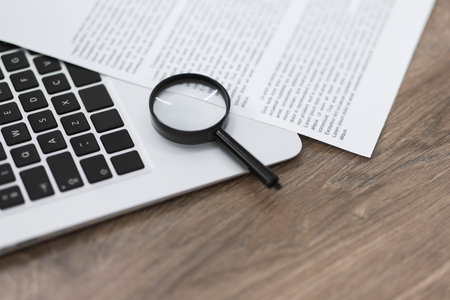 Magnifying glass, laptop and document on wooden table, closeupの写真素材