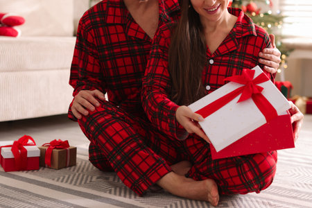 Happy couple in pajamas with Christmas gift at homeの写真素材