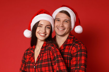 Happy couple in Santa hats and pajamas on red background. Christmas atmosphereの写真素材