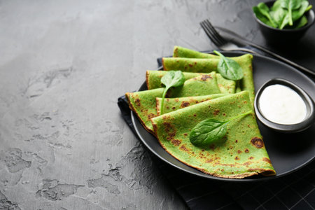 Tasty spinach crepes with sour cream and leaves on black table, closeup. Space for textの写真素材