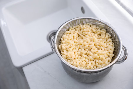 Sieve with pasta on pot in kitchen, closeup. Space for textの写真素材