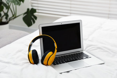 Stylish headphones and laptop on bed indoorsの写真素材