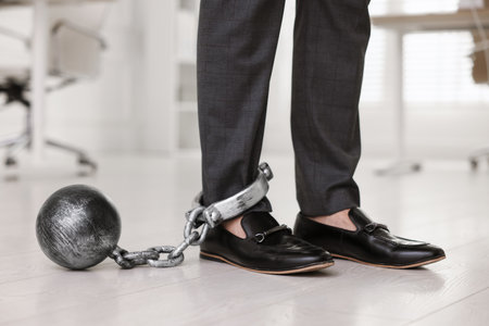 Businessman with metal ball and chain on his leg in office, closeupの写真素材