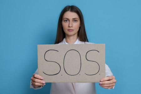 Businesswoman holding sign with word SOS on light blue background