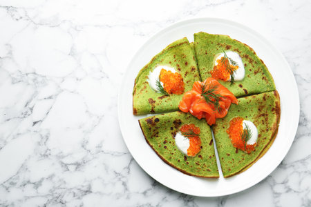 Tasty spinach crepes with salmon, red caviar, sour cream and dill on white marble table, top view. Space for textの写真素材
