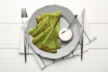 Tasty spinach crepes and sour cream on white wooden table, flat layの写真素材
