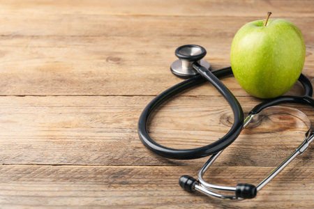 Ripe apple and stethoscope on wooden table, closeup. Space for textの写真素材