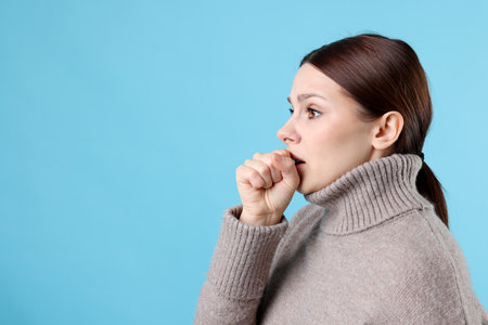 Woman coughing on light blue background, space for text. Cold symptomの写真素材