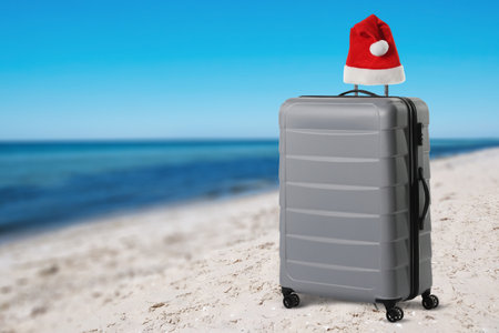 Suitcase with Santa hat on sandy beach near seaの写真素材