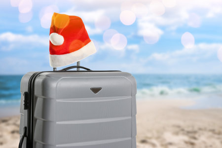 Suitcase with Santa hat on sandy beach near seaの写真素材