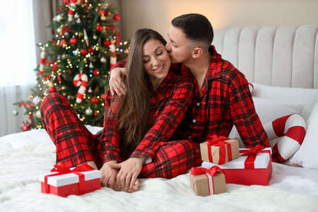 Happy couple in pajamas with Christmas gifts on bed at homeの写真素材