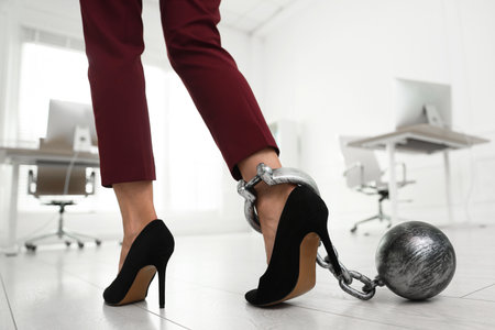 Businesswoman with metal ball and chain on her leg indoors, closeupの写真素材