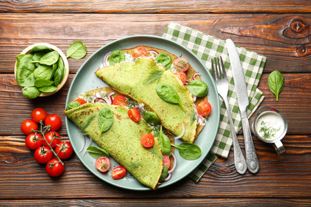 Tasty spinach crepes with tomatoes, onion, sour cream and leaves on wooden table, flat layの写真素材