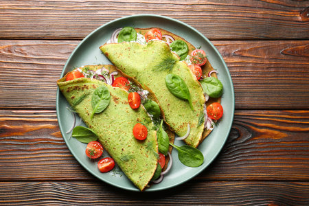 Tasty spinach crepes with tomatoes, onion, sour cream and leaves on wooden table, top viewの写真素材