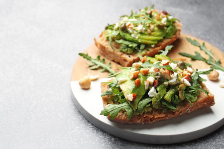 Tasty bruschettas with avocado, arugula, nuts and feta cheese on gray table, closeup. Space for textの写真素材