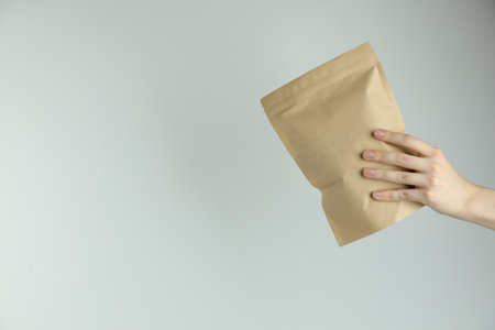 Woman with stand-up pouch on light gray background, closeup. Space for textの写真素材