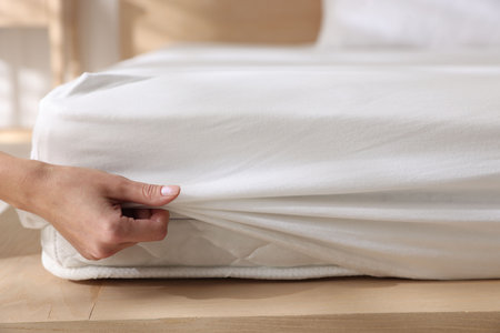 Woman putting bed sheet on mattress indoors, closeup