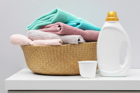 Laundry basket with towels, bottle of detergent and cap on dresser near white wall indoors, closeupの写真素材