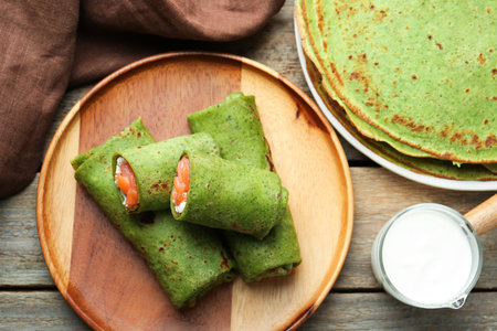 Tasty spinach crepes with salmon and cream cheese served on wooden table, flat layの写真素材