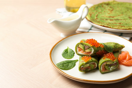 Tasty spinach crepes with salmon, avocado and red caviar served on wooden table, closeup. Space for textの写真素材
