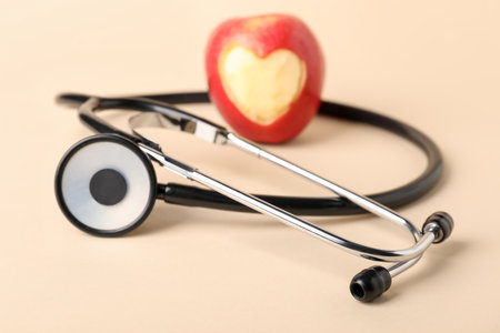 Ripe apple with carved heart and stethoscope on beige background, closeupの写真素材