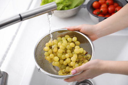 Woman washing grapes in sieve at kitchen, closeupの写真素材
