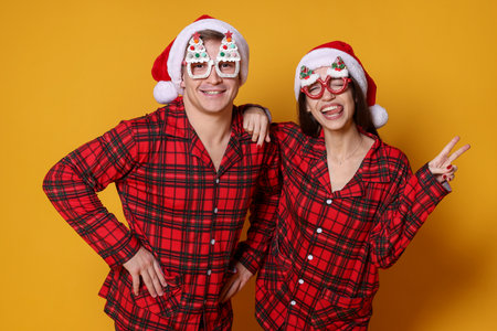 Happy couple in Santa hats, funny glasses and pajamas on orange background. Christmas atmosphereの写真素材