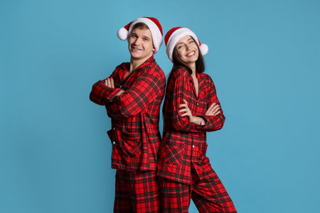 Happy couple in Santa hats and pajamas on light blue background.の写真素材