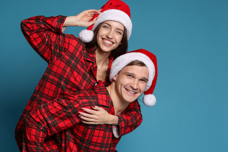 Happy couple in Santa hats and pajamas on light blue background. Christmas atmosphereの写真素材