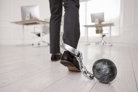 Businessman with metal ball and chain on his leg in office, closeupの写真素材
