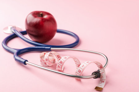 Ripe apple, measuring tape and stethoscope on pink background, closeupの写真素材