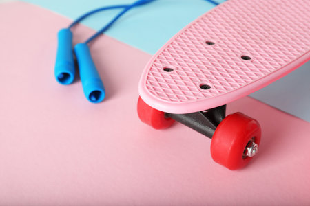 Bright penny board and skipping rope on color background, closeup