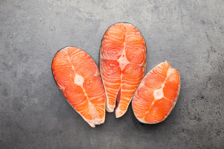 Pieces of salmon fillet on gray textured table, flat lay