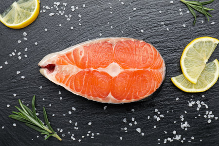 Piece of salmon fillet with spices and lemon on black textured table, flat lay