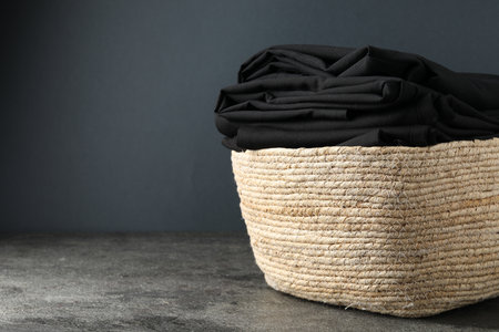 Laundry basket with clothes on gray textured table against dark background, closeup. Space for textの写真素材