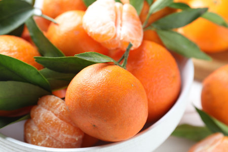 Fresh tangerines and green leaves in bowl on table, closeupの写真素材