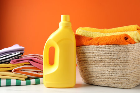 Laundry basket with towels, clothes and bottle of detergent on light table near orange wall indoors, closeupの写真素材