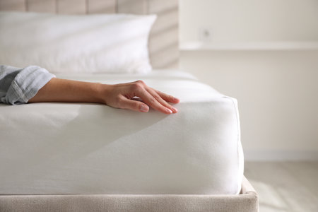 Woman touching soft mattress on bed indoors, closeup. Space for text