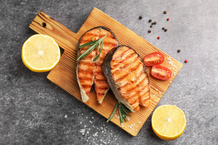 Tasty grilled salmon steaks served with lemon, tomatoes and rosemary on gray table, flat layの写真素材