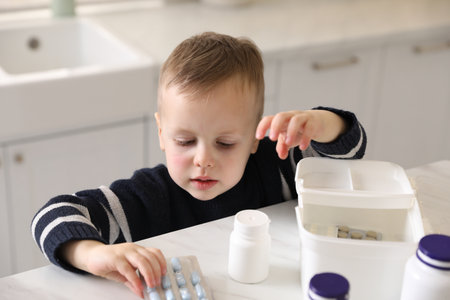 Child safety at home. Little boy playing with pills at table in kitchenの写真素材
